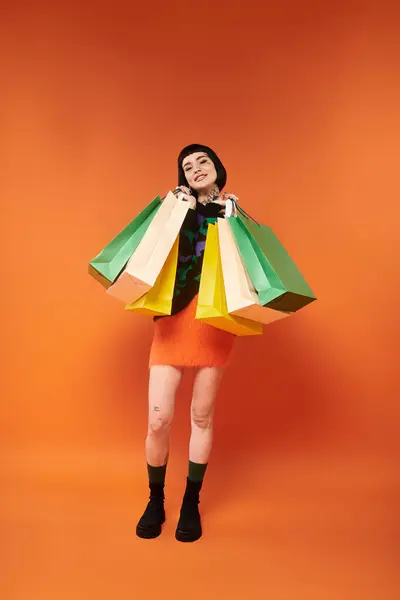 Brightly dressed in a vibrant sweater, she joyfully displays her shopping haul in studio lighting. — Stock Photo