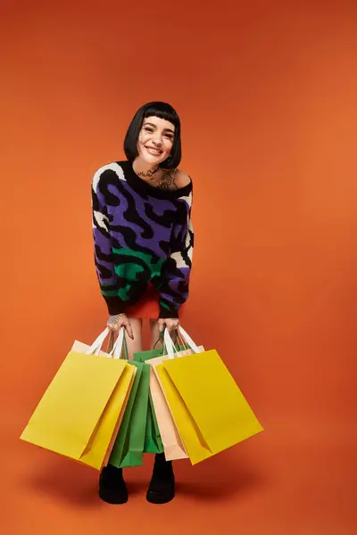Brightly dressed in a colorful sweater, a young woman joyfully holds shopping bags, radiating happiness. — Stock Photo