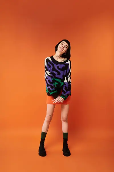 A young woman with tattoos and stylish short hair smiles brightly while wearing a colorful sweater in a studio. — Stock Photo