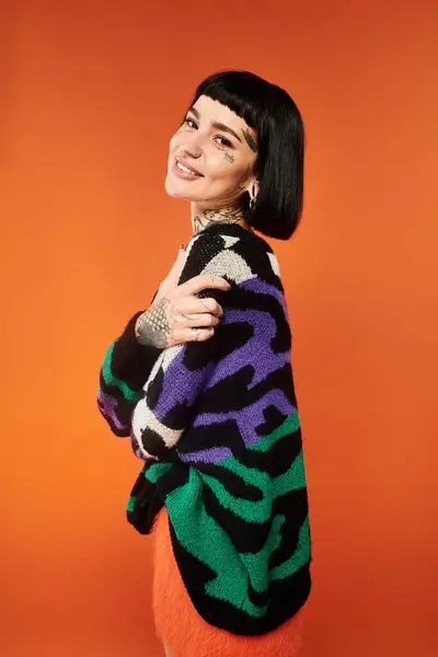 A vibrant young woman with short hair and tattoos smiles in a playful studio, showcasing her bright sweater. — Stock Photo
