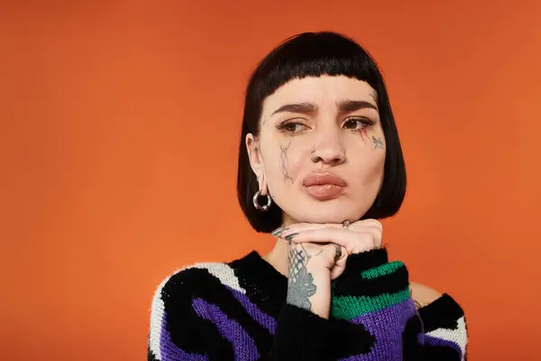 Una mujer joven con un diseño de tatuaje único y modelos de pelo corto un suéter brillante en un entorno de estudio llamativo. — Stock Photo