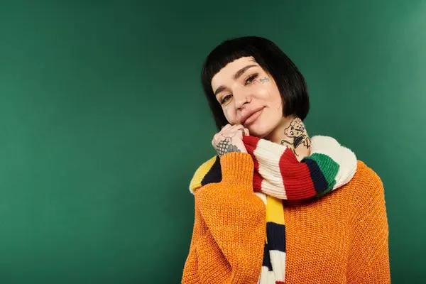 A young woman dressed in a warm sweater and colorful scarf poses warmly, showcasing her tattoos. — Stock Photo