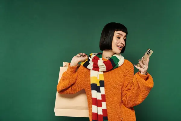 A joyful young woman with short hair and tattoos smiles at her phone while dressed in a warm sweater. — Stock Photo