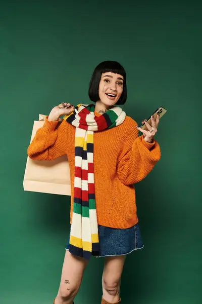 A young woman with short hair and tattoos smiles joyfully, dressed in a cozy sweater and colorful scarf. — Stock Photo