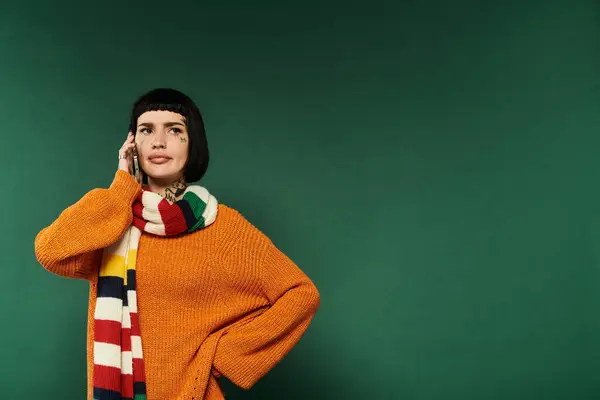 Une jeune femme pose en toute confiance dans un pull chaud, ses tatouages visibles, entourée d'un décor de studio vert. — Photo de stock