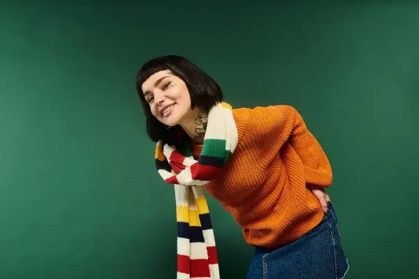 A young woman with short hair and vibrant tattoos poses in a warm sweater against a rich green backdrop. — Stock Photo