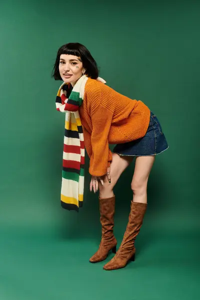 A young woman with short hair shows off her tattoos while wearing a warm, cozy sweater in a studio. — Stock Photo