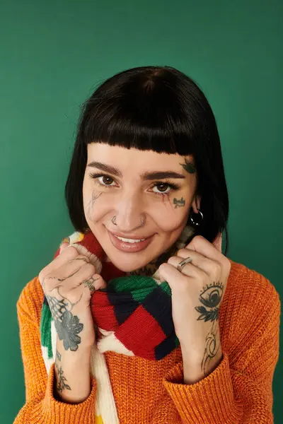 A young woman with tattoos joyfully poses in a cozy sweater, radiating warmth against a green backdrop. — Stock Photo
