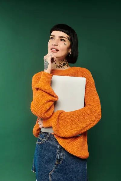 Una giovane donna con i capelli corti e tatuaggi tiene un computer portatile mentre indossa un caldo, accogliente maglione. — Foto stock