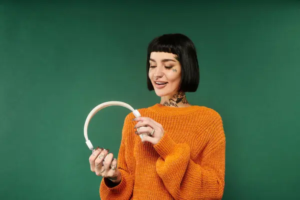 A young woman with short hair and tattoos smiles as she holds a stylish accessory, embracing the cozy warmth. — Stock Photo