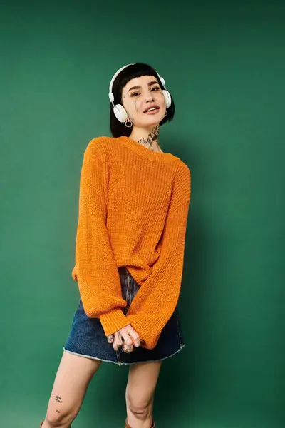 A young woman with short hair and tattoos wears a cozy orange sweater while striking a playful pose. — Stock Photo