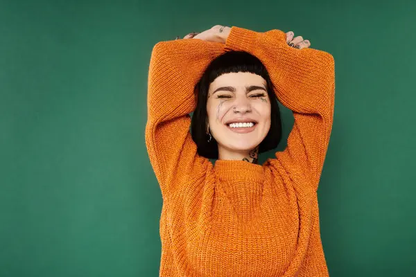 A young woman with short hair and tattoos brings life to the studio with her joyful pose in a cozy sweater. — Stock Photo