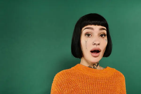 A tattooed young woman wearing a warm sweater showcases an expression of surprise in a studio setting. — Stock Photo