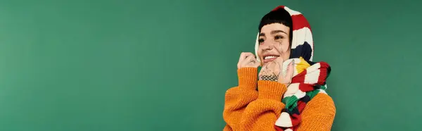 Radiating joy, a young woman in a colorful sweater and scarf poses with a playful smile on a green backdrop. — Stock Photo