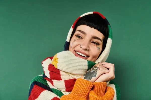 A cheerful young woman with short hair and tattoos poses in a snug sweater and scarf, radiating warmth and joy. — Stock Photo