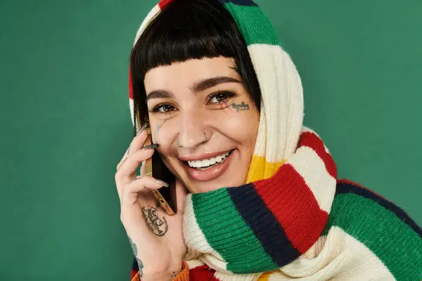 Eine junge Frau mit kurzen Haaren und Tätowierungen strahlt glücklich, während sie in einem gemütlichen Rahmen einen bunten Pullover und Schal trägt.. — Stockfoto