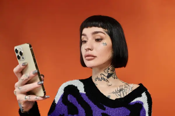 A young woman with short hair and tattoos enjoys her time holding a smartphone in a studio setting. — Stock Photo