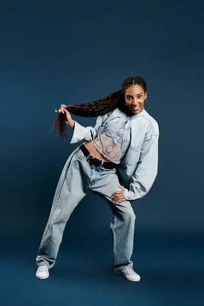 A stylish young woman poses playfully in fashionable attire against a blue background. — Stock Photo