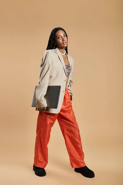 A young woman showcases her fashion sense, confidently holding a laptop in a vibrant outfit. — Stock Photo