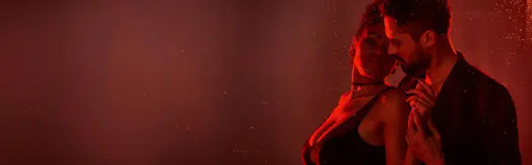 A couple shares an intimate moment, surrounded by captivating red light and droplets of water. — Stock Photo