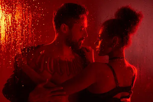 Una coppia amorevole condivide un momento tenero, illuminato da luce rossa morbida e acqua a cascata. — Foto stock