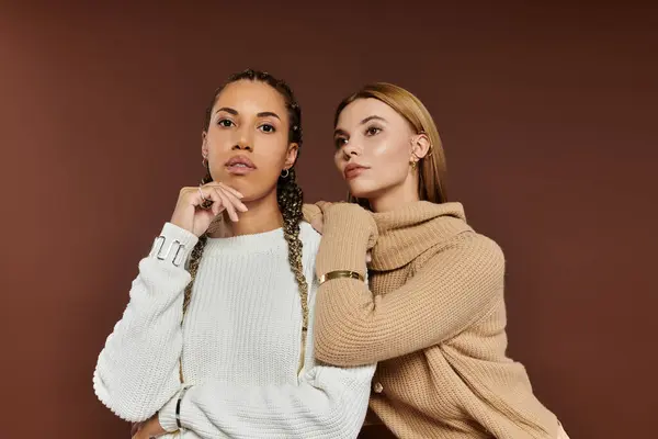 Two young women in stylish autumn attire share a tender moment against a warm backdrop. — Stock Photo