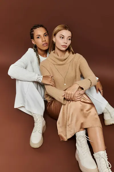 Una pareja de lesbianas con estilo se sienta cerca, compartiendo calidez en trajes suaves de otoño. - foto de stock