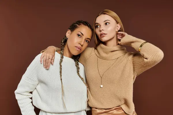Two young women share a tender moment, dressed in chic autumn attire against a warm backdrop. — Stock Photo