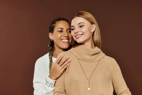 Two young women embrace warmly, smiling in their stylish autumn outfits against a cozy backdrop. — Stock Photo