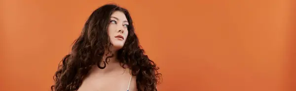 A young woman with beautiful curls showcases her style on a vibrant orange background. — Stock Photo