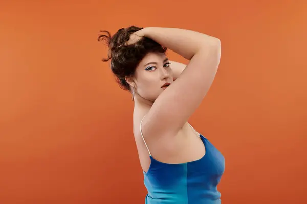 Красивая женщина plus size уверенно позирует в потрясающем синем платье, излучая очарование в студии. — стоковое фото