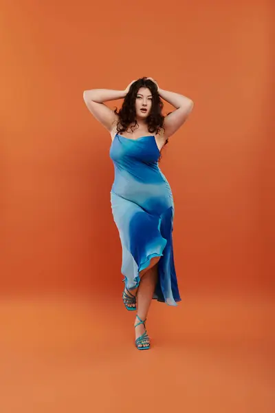 A young and beautiful plus size woman showcases her vibrant blue dress while striking a pose in a studio setting. — Stock Photo