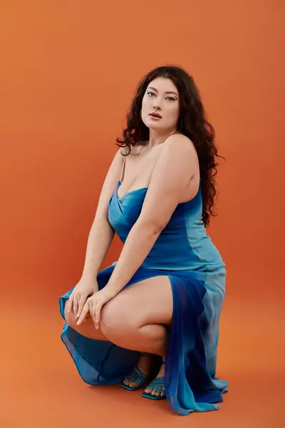 A young, beautiful plus size woman showcases a stunning blue dress while confidently posing in a studio setting. — Stock Photo