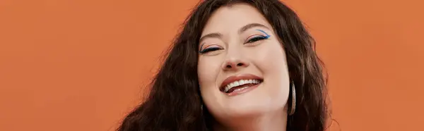 A joyful plus size woman showcases her style, smiling brightly on a lively orange background. — Stock Photo