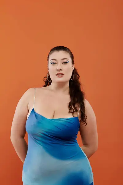 A confident young woman in a stunning blue dress showcases her beauty with makeup, radiating charm. — Stock Photo
