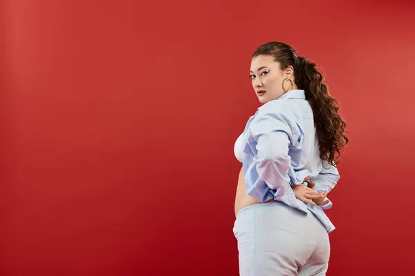 A young plus size woman showcases her confidence with bright makeup while posing against a bold red background. — Stock Photo