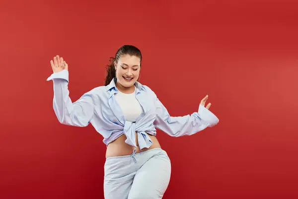 A vibrant plus-size woman radiates confidence with bold makeup against a striking red backdrop. — Stock Photo