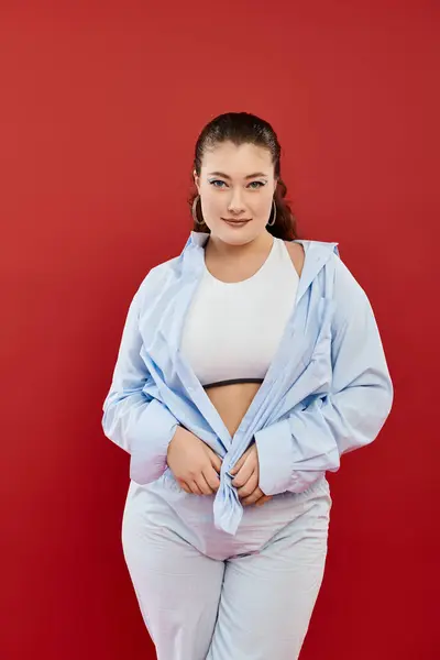 A plus size woman with stylish makeup exudes confidence while posing in a vibrant red studio environment. — Stock Photo