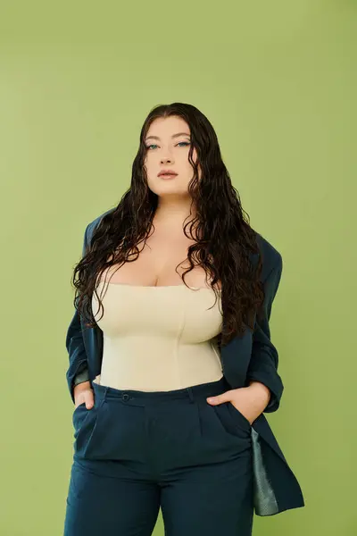 A young plus size woman with curly hair confidently poses in a stylish suit against a lively green background. — Stock Photo
