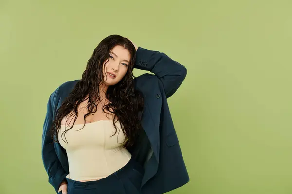 A stunning plus size woman with curly hair showcases her style in a chic suit, standing on a green backdrop. — Stock Photo