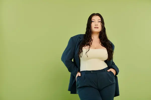 A young, beautiful plus-size woman with curly hair flaunts her style in a suit against a vibrant green backdrop. — Stock Photo