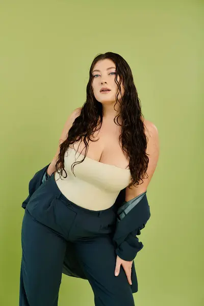 Una hermosa mujer de talla grande muestra su cabello rizado y su estilo confiado en un traje elegante mientras toma una pose. - foto de stock
