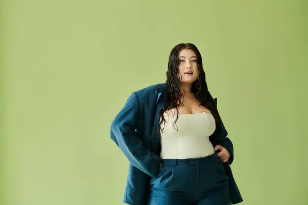 A confident, beautiful plus-size woman with curly hair models a striking suit against a green backdrop. — Stock Photo