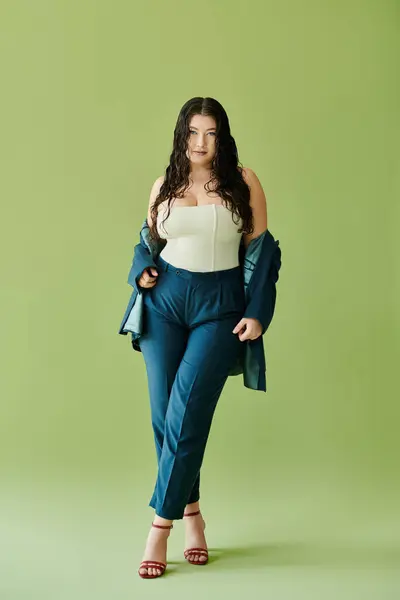 A confident plus-size woman with curly hair showcases her stylish suit in a studio with a bright green background. — Stock Photo