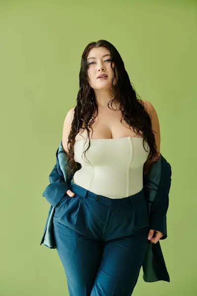 A young beautiful woman with curly hair showcases her fashion sense in a tailored suit on a bright green backdrop. — Stock Photo