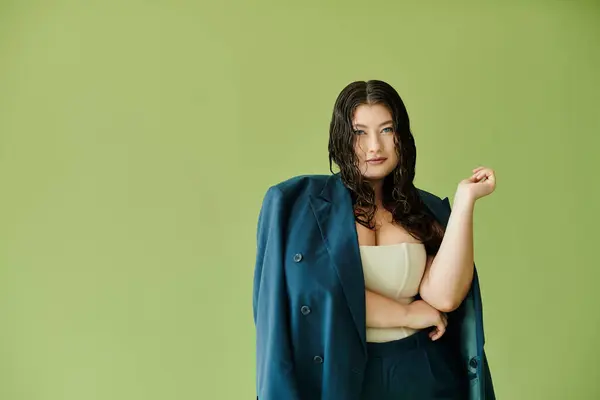 A beautiful plus-size woman in a suit stands gracefully, her curly hair complementing a vibrant green backdrop. — Stock Photo