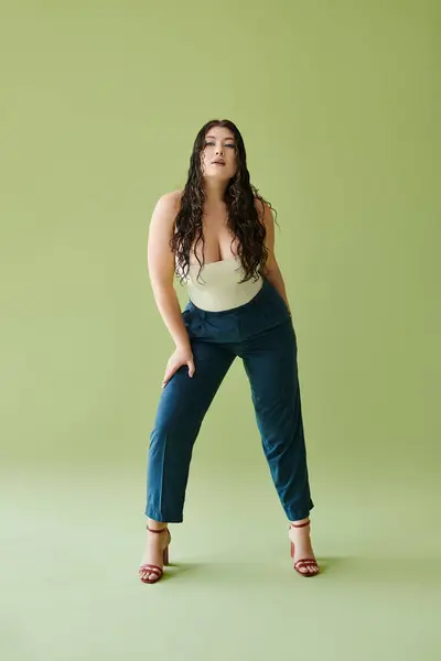 A confident young plus-size woman in a corset stands against a vivid green backdrop with curly hair. — Stock Photo
