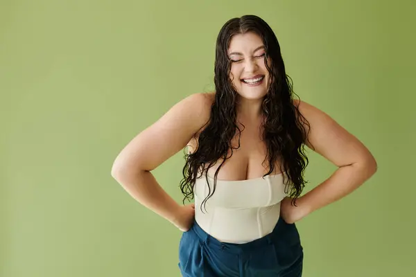 A joyful plus size woman with curly hair showcases her confidence in a stylish corset on a bright green backdrop. — Stock Photo