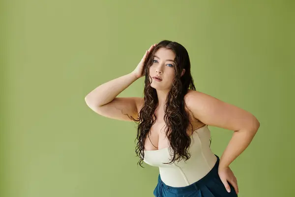 A stunning plus size model with curly hair gracefully poses in a corset, shining against a luscious green background. — Stock Photo