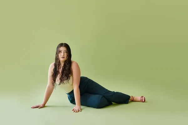 A beautiful plus size woman poses confidently in a corset and stylish pants against a rich green background. — Stock Photo